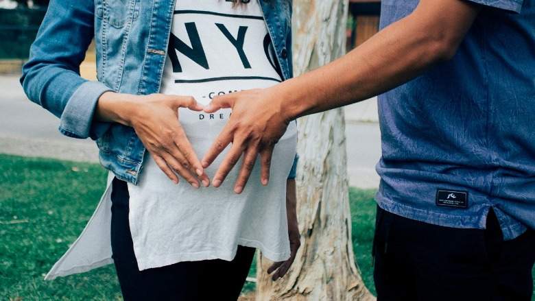 A man and a woman holding a handmade heart over a woman's pregnant belly.