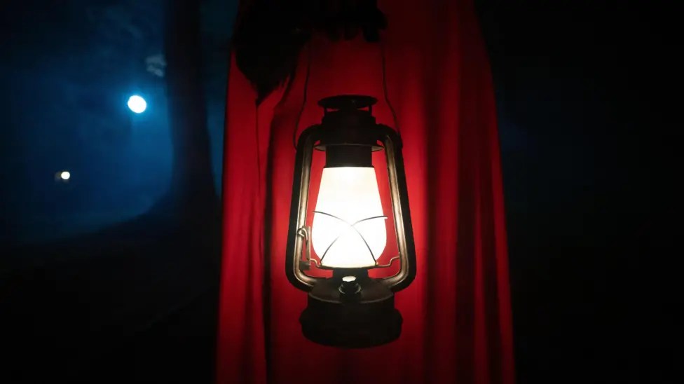 The Secret Traitor in a red cloak holding a lamp.