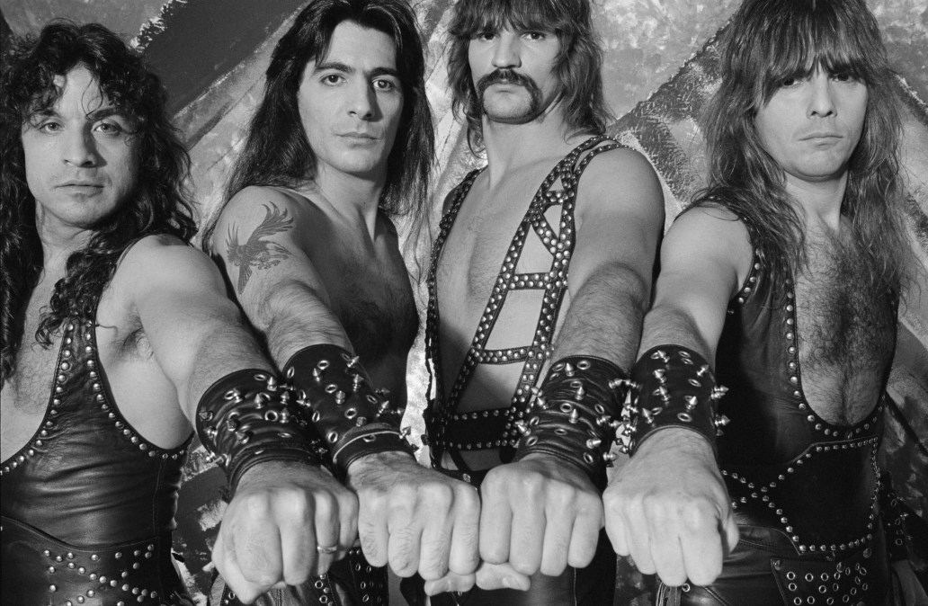Manowar (drummer Scott Columbus (1956-2011), guitarist Ross Friedman, bassist Joey DeMaio and singer Eric Adams), US heavy metal band, wearing their stage costumes of studded black leather, each holding out a hand wearing a studded black leather cuff, for a group studio portrait in London, England, Great Britain, 1986.