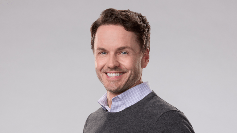 Paul Campbell smiles in sweater and white button down shirt